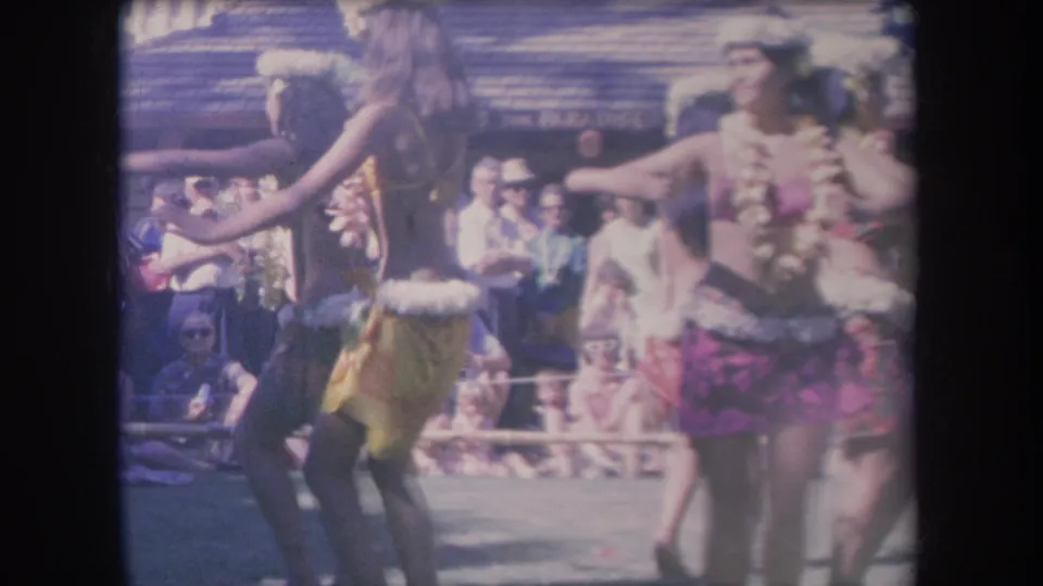 Handheld 8mm Hawaii frame from 1969 showing dancers moving across an outdoor performance area before spectators.