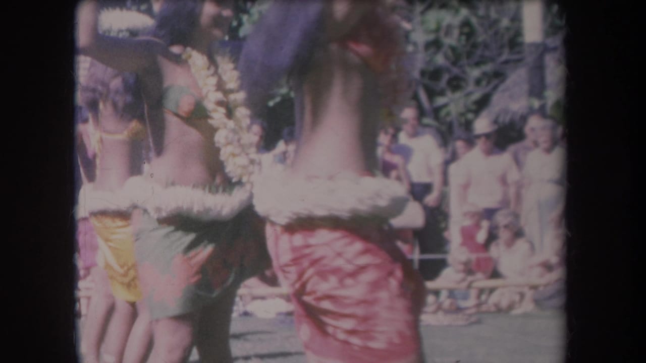1969 Hawaii home-movie frame showing young women hula dancing in leis and skirts before an outdoor audience.