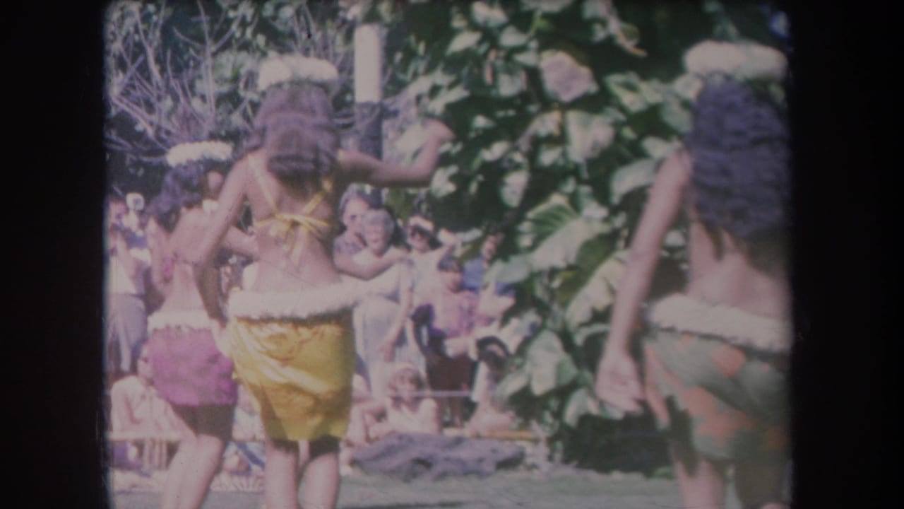 Women in grass-style skirts dance before an outdoor audience.