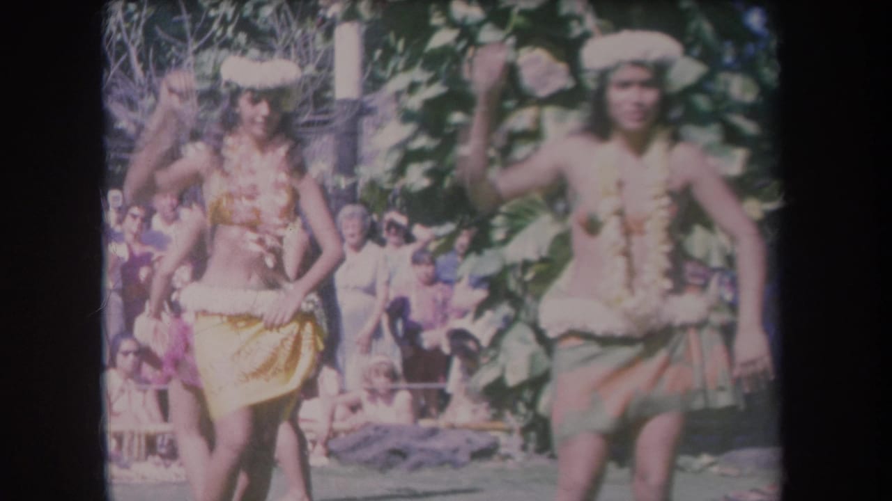 1969 Hawaii frame showing two women in traditional-style dance costumes performing outdoors before an audience.