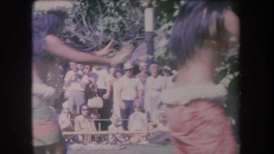 1969 Hawaii frame with a dancer near the lens and an outdoor audience visible beyond the performance area.