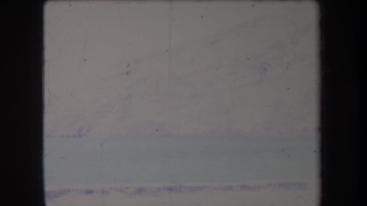1969 Hawaii 8mm frame showing a soft, distant snowy mountain or ridge above a pale flat foreground.