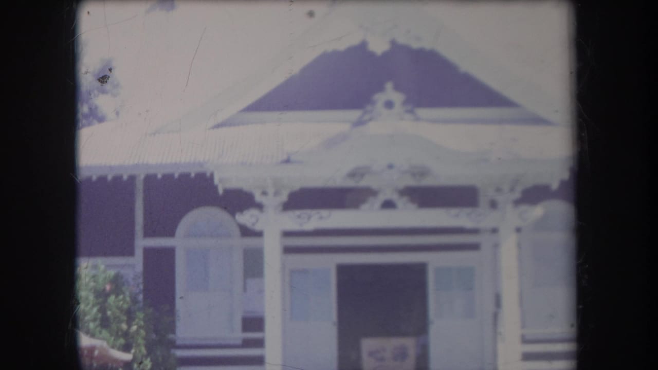 1969 Hawaii home-movie frame of a decorative house front with gabled roof, white trim, porch posts, and an open central doorway.