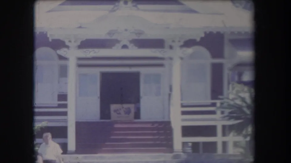 1969 Hawaii 8mm frame showing the front steps and open doorway of a decorative house, with plants and a person partly visible below.