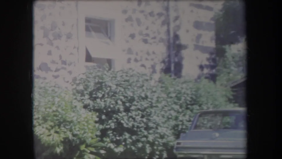 1969 Hawaii residential exterior with apartment windows, lush shrubs, and the rear portion of a parked 1960s car.