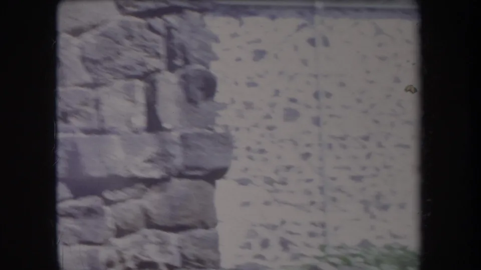 1969 Hawaii 8mm frame showing rough rockwork beside a pale stone or stucco wall, with soft focus and visible film grain.