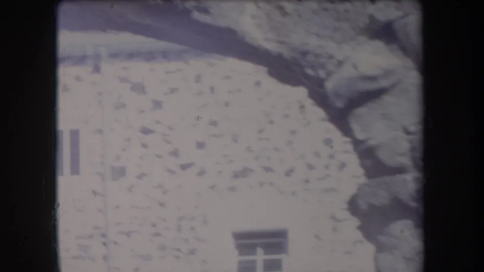 1969 Hawaii 8mm frame showing a curved rock arch near a stone building wall with small windows and palm foliage.