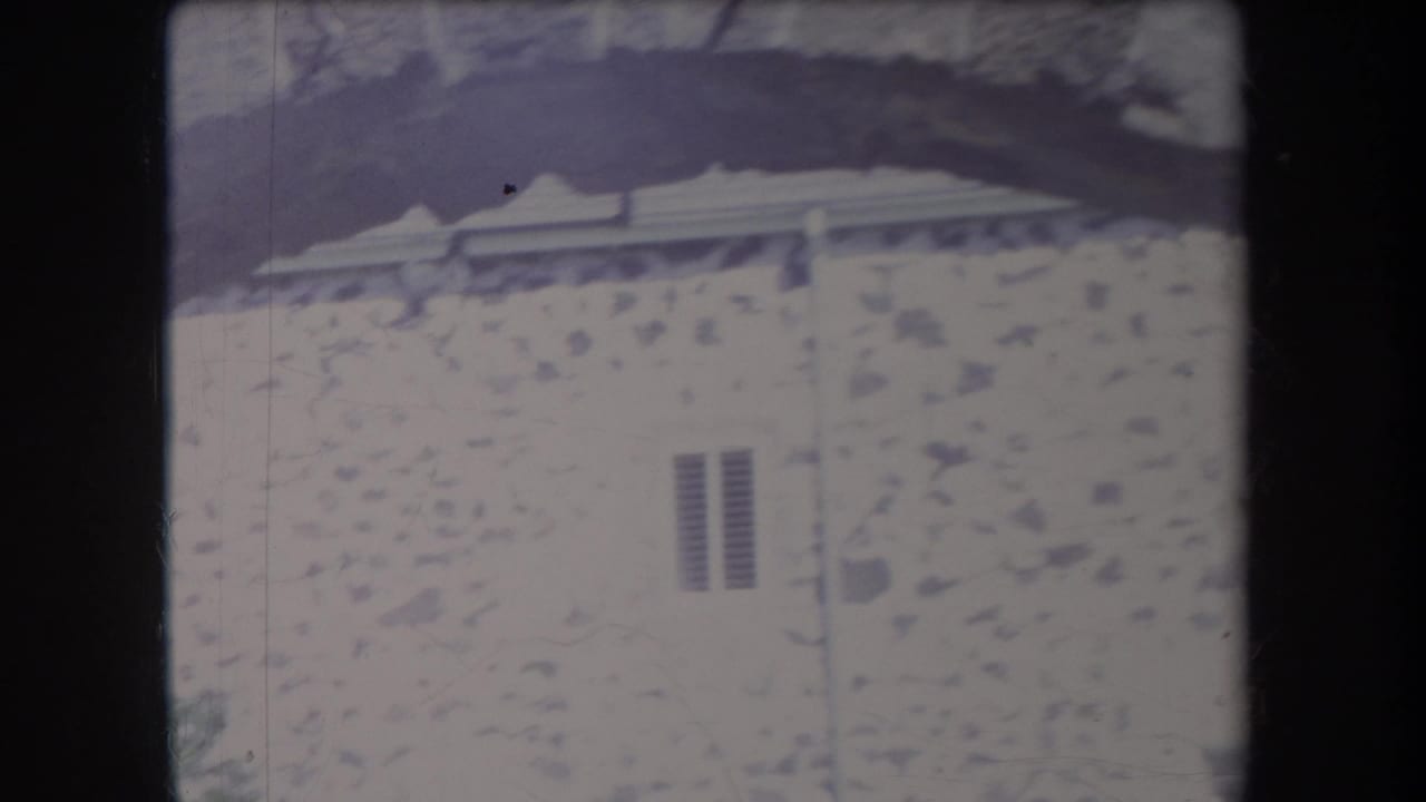 1969 Hawaii 8mm frame showing a pale stone church wall, small louvered window, and nearby tree shade.