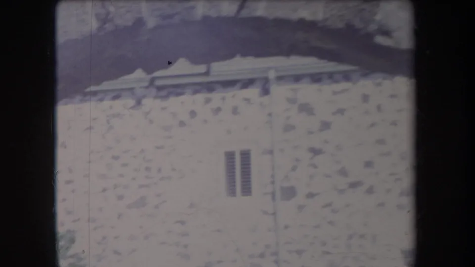1969 Hawaii 8mm frame showing a pale stone church wall, small louvered window, and nearby tree shade.