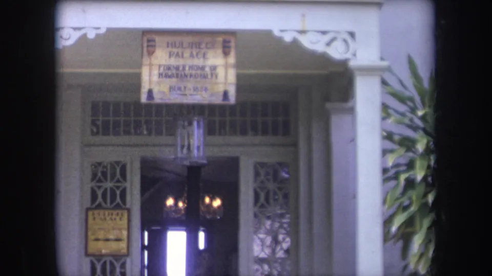 1969 Hawaii 8mm frame showing the Hulihee Palace entrance with a hanging sign, white columns, latticework, and plants at the side.