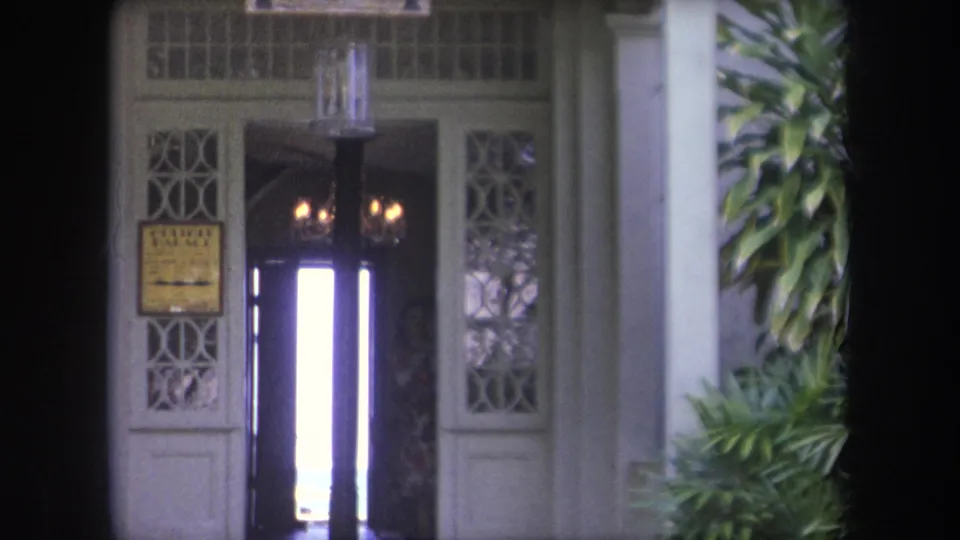 1969 Hawaii 8mm view of the Hulihee Palace doorway, showing a yellow entrance sign, decorative side panels, and bright light through the door.