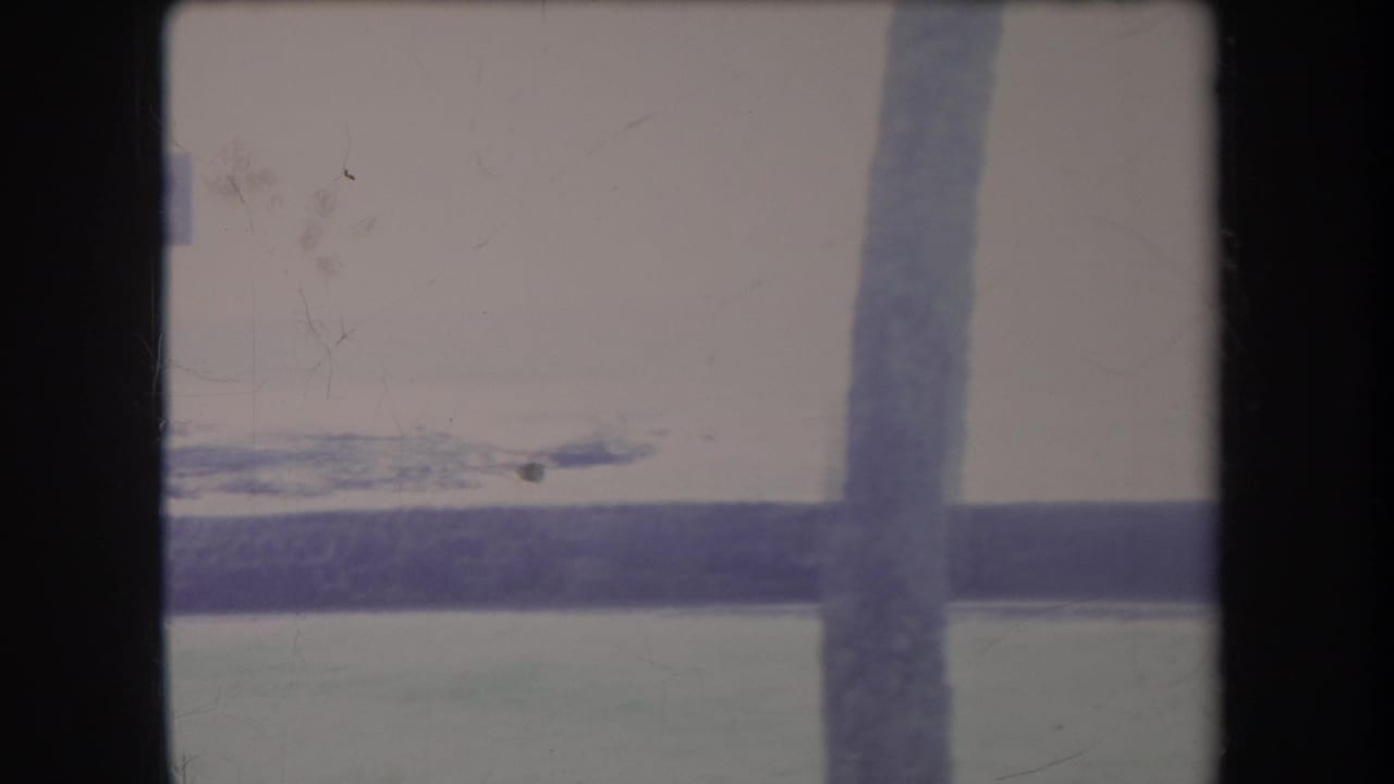 1969 Hawaii 8mm frame looking across calm water, with a distant shoreline seen through dark shelter or window framing.