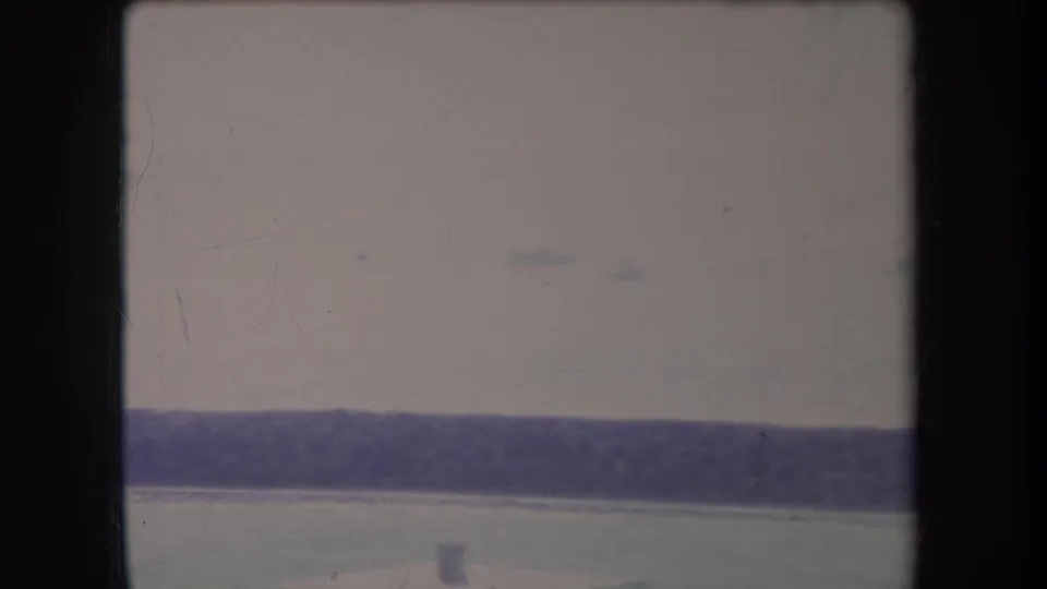 Overexposed 1969 Hawaii 8mm frame showing calm water and distant marks beyond dark foreground rails.
