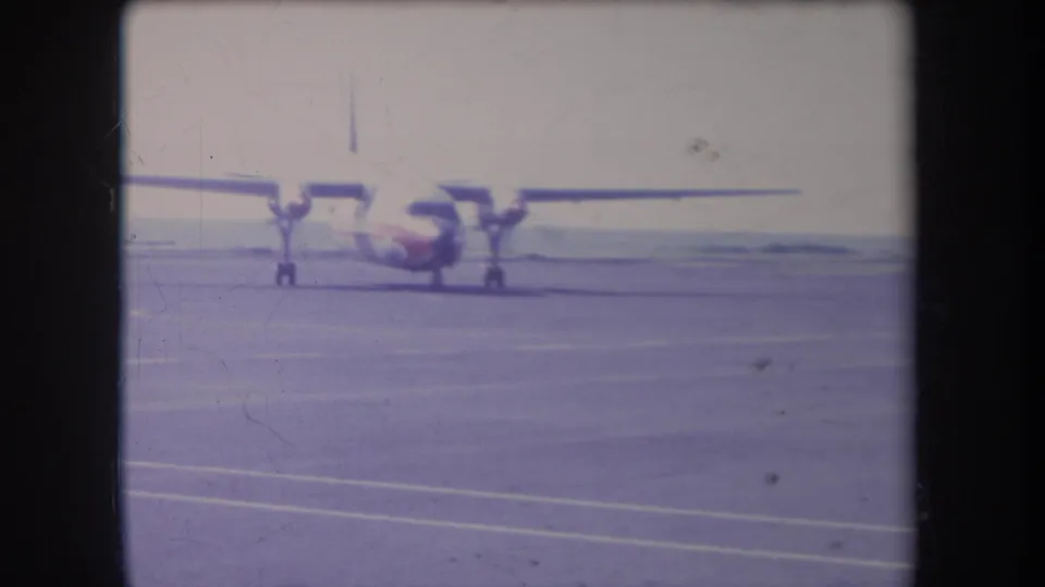 1969 Hawaii 8mm frame showing a small propeller aircraft on runway pavement, seen from a distant home-movie viewpoint.