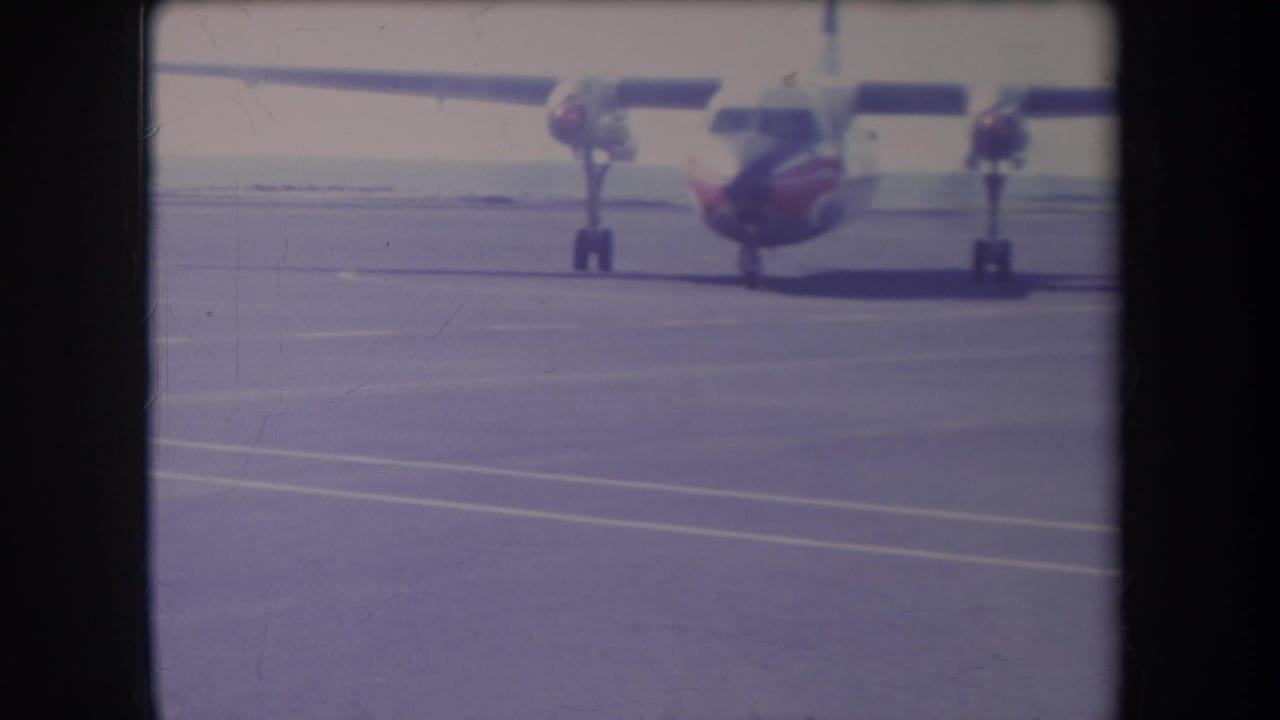 1969 Hawaii 8mm frame showing a small red-and-white propeller airplane parked or moving on a wide airport tarmac.