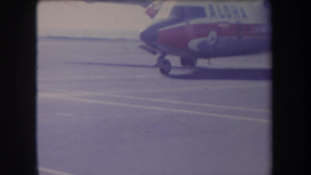 Partial nose of a red-and-white airplane beside open tarmac.