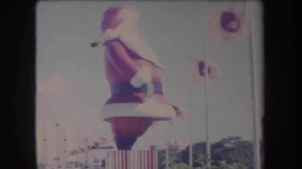 Faded 8mm Hawaii holiday scene showing a large inflatable Santa Claus figure near flags, buildings, and airport-area landscaping.