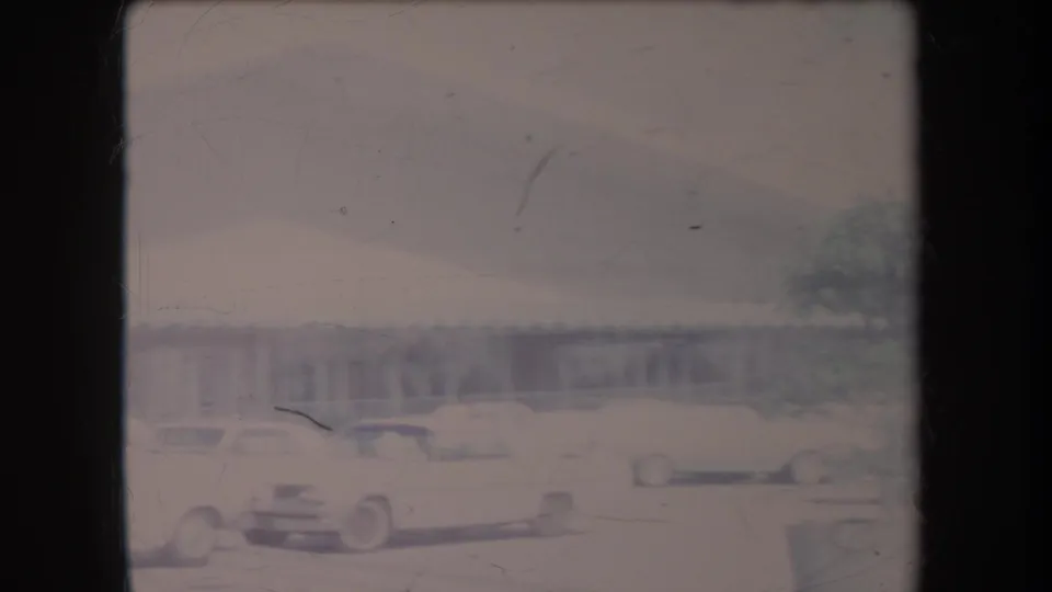 1969 Hawaii frame showing a white station wagon and other cars near a long low building, with soft focus and visible film wear.
