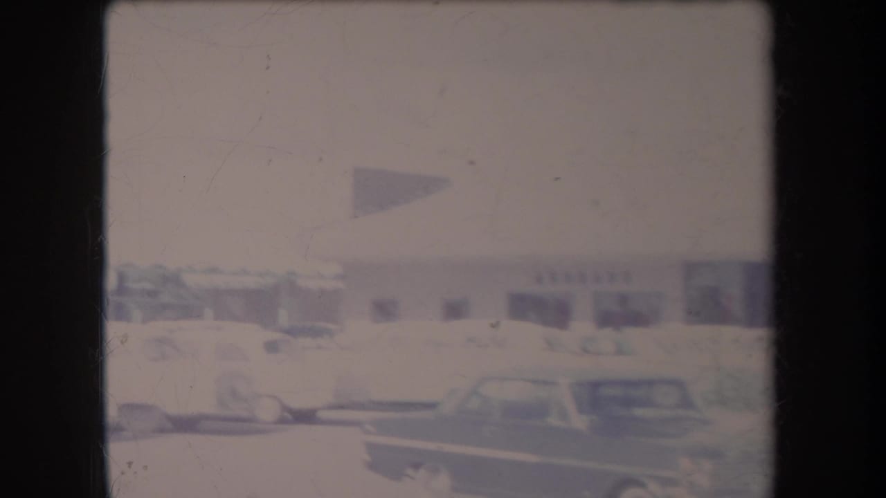Soft 8mm view of parked classic cars beside a one-story commercial building in Hawaii, dated by metadata to 1969.