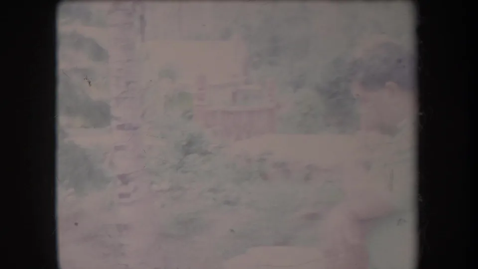 A man in a light-colored shirt appears seated outdoors in 1969 Hawaii, seen softly through faded 8mm color and scratches.