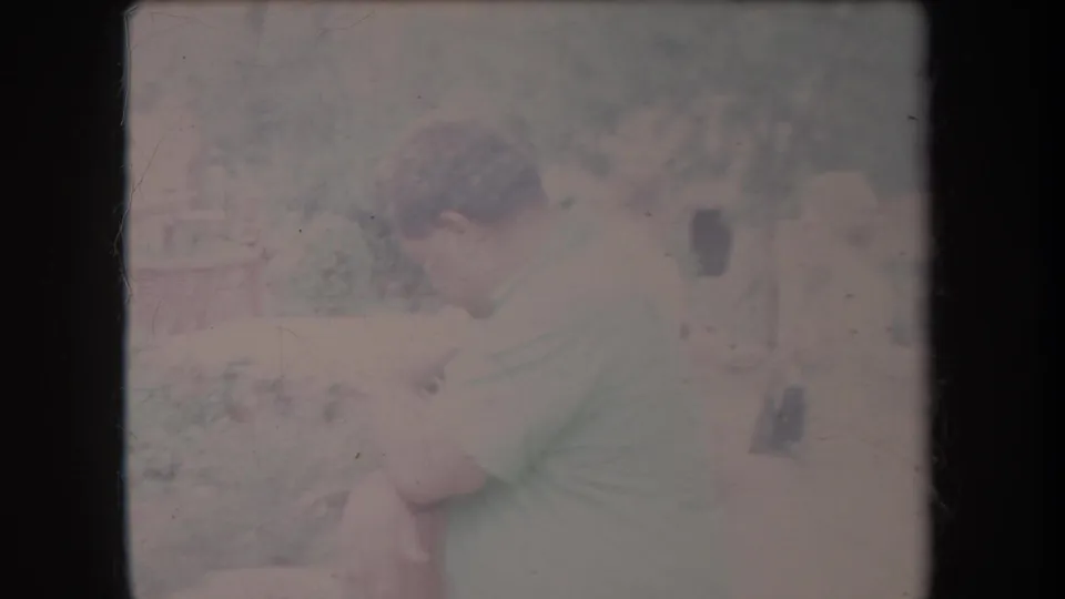 Profile view of an adult man seated outdoors in Hawaii, appearing contemplative amid foliage in faded 1969 8mm footage.