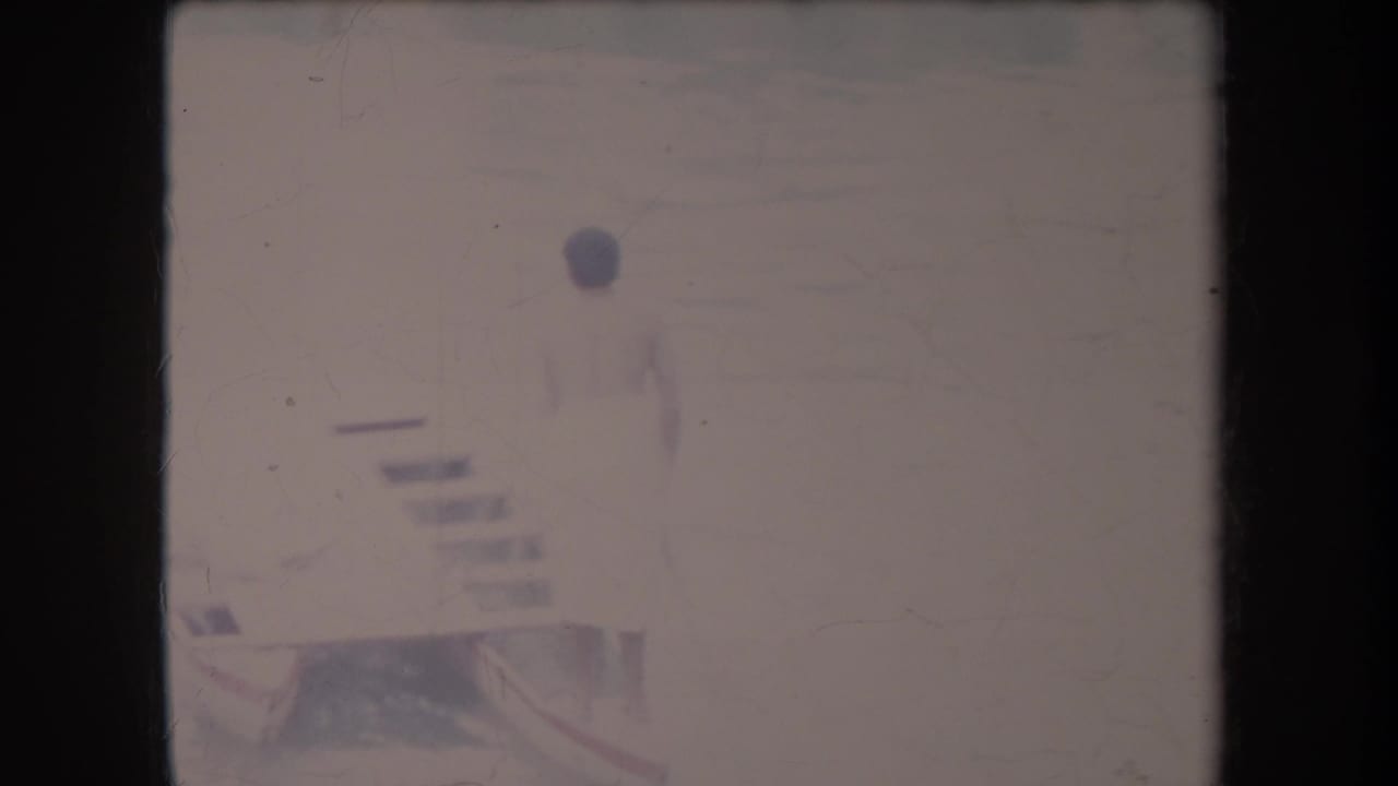 Person in a light swimsuit standing near a pool edge or dock in a faded 8mm frame.