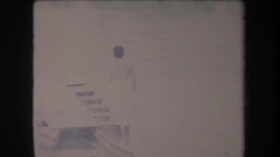 1969 Hawaii home-movie frame showing a person in a light swimsuit by a resort pool edge, partly obscured by faded exposure and film wear.