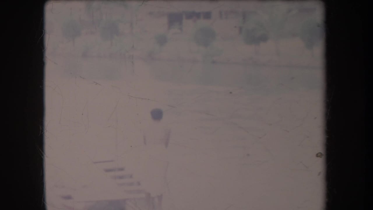 Person in a light swimsuit beside pool water with resort landscaping faintly visible.