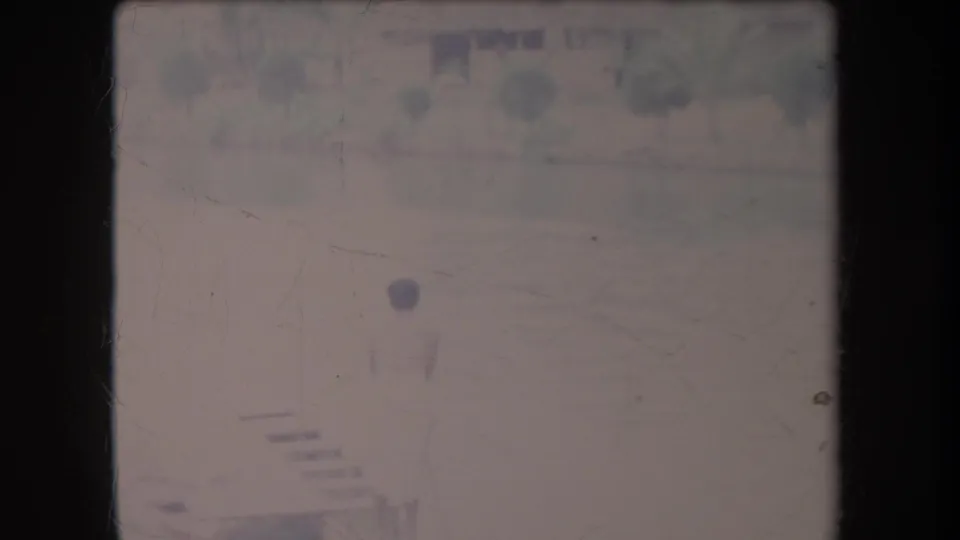 Faded 1969 Hawaii vacation frame with a person near the pool area and soft outlines of landscaping or structures behind them.