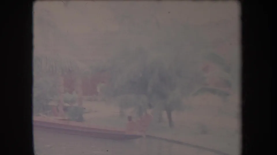 1969 Hawaii home-movie frame showing the pool area, palms, and a person near the water in a soft, faded 8mm scan.