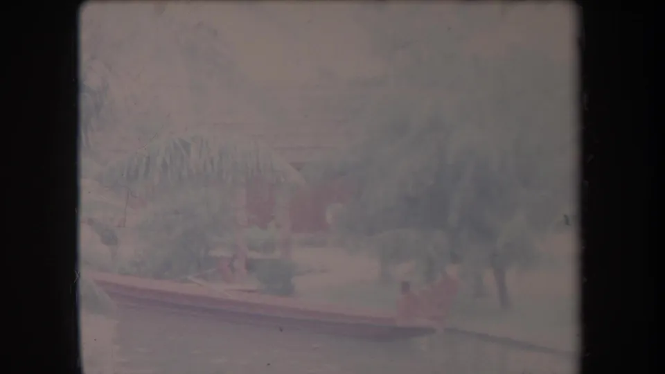 1969 Hawaii 8mm frame showing a small outrigger canoe moving along calm tropical water beneath palm fronds.