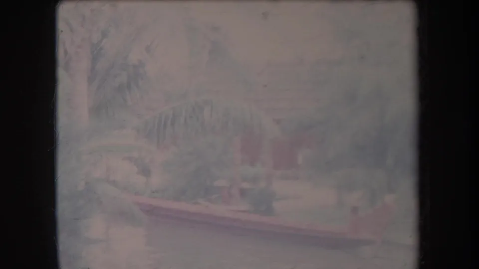 Faded 1969 Hawaii home-movie frame with an outrigger canoe along a quiet river bordered by palm trees and greenery.