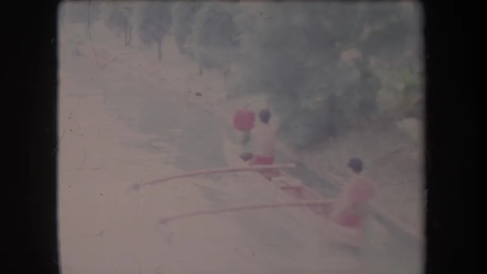 At the end of the clip, the two men and their small outrigger canoe appear farther down the canal, partially softened by exposure and grain.