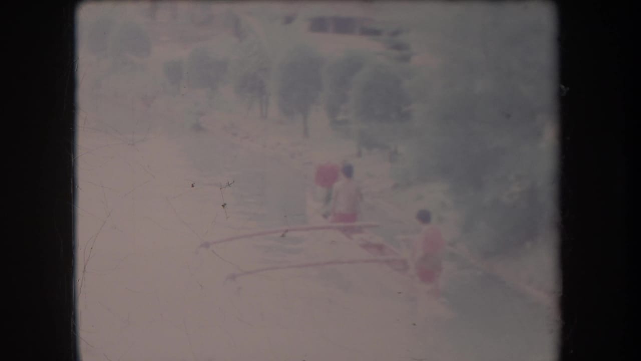 Faded 8mm frame from Hawaii showing the canoe farther along the river, with three paddlers visible against soft trees.