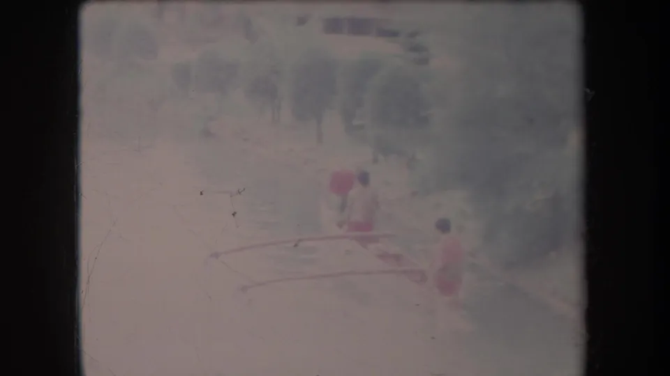 Faded 8mm frame from Hawaii showing the canoe farther along the river, with three paddlers visible against soft trees.