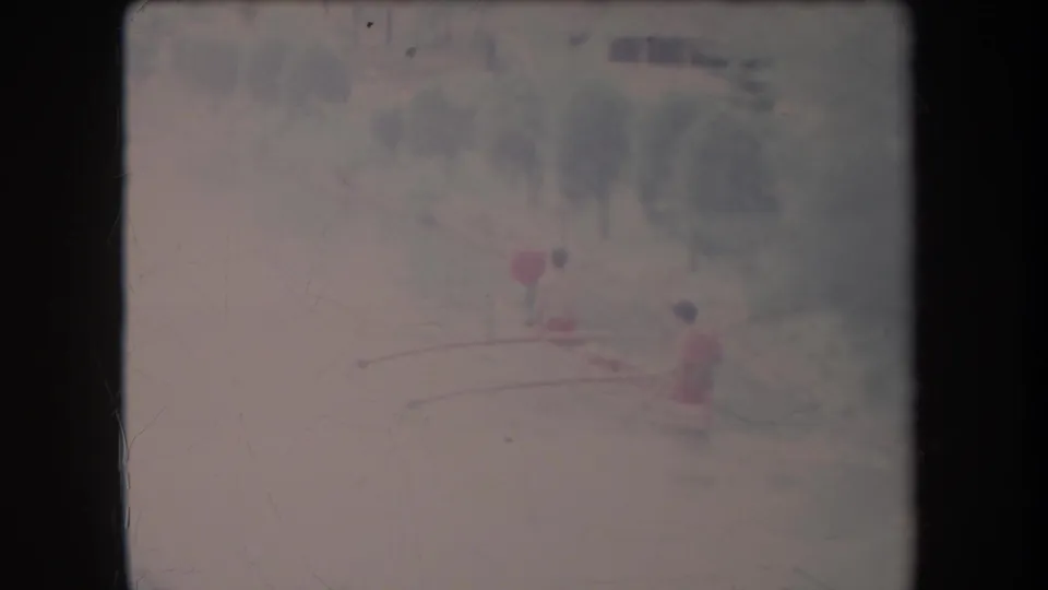 1969 Hawaii 8mm frame with three distant people paddling an outrigger-style canoe across a hazy river scene.