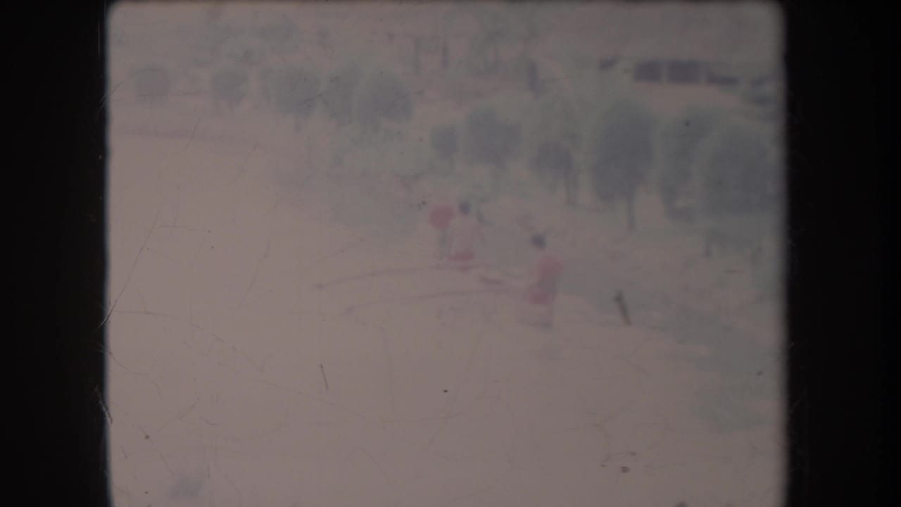 1969 Hawaii 8mm frame showing a distant small boat with red-shirted figures on pale, hazy water near trees.