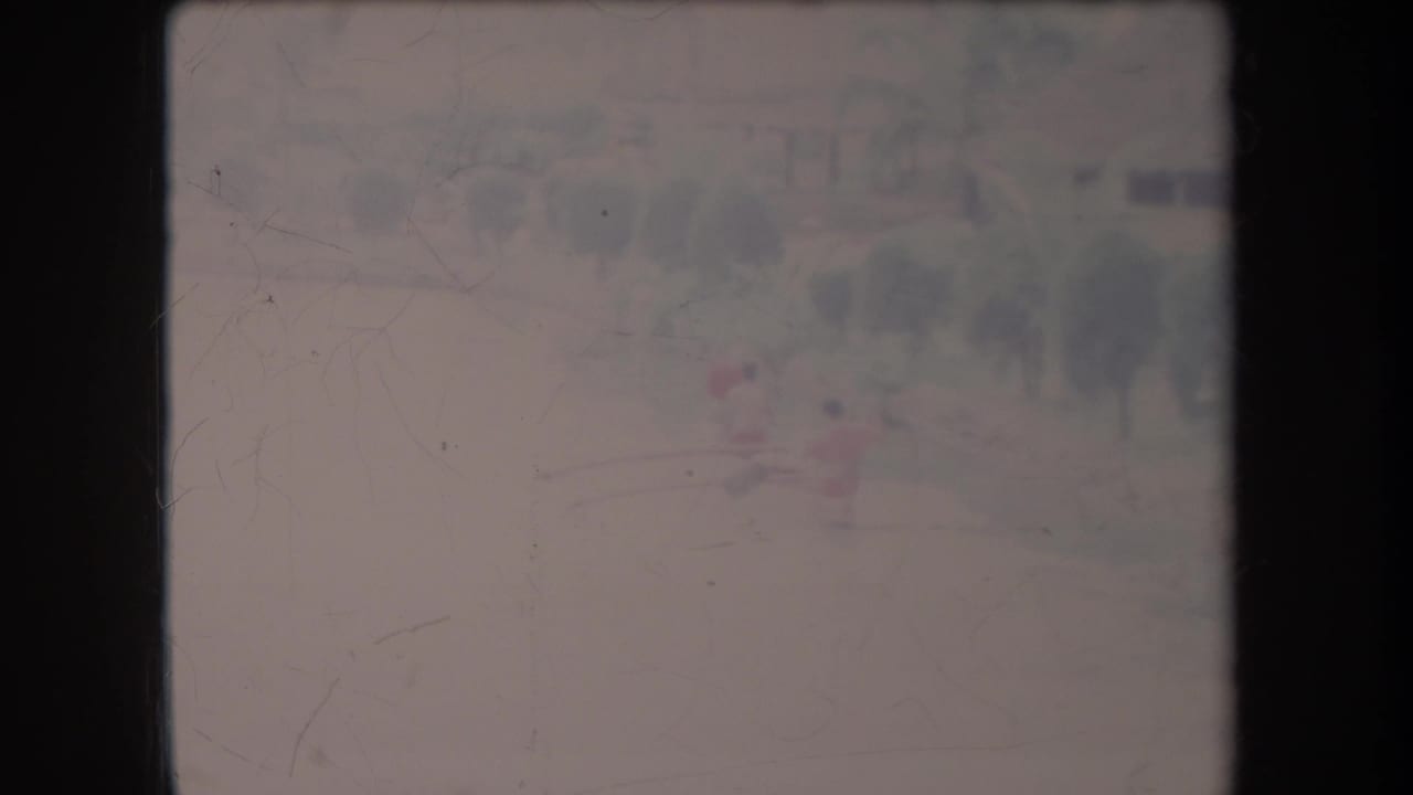Faded 1969 Hawaii home-movie frame with two distant figures in a small boat on calm water before a soft tree line.