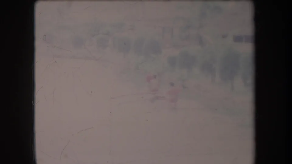 Faded 1969 Hawaii home-movie frame with two distant figures in a small boat on calm water before a soft tree line.