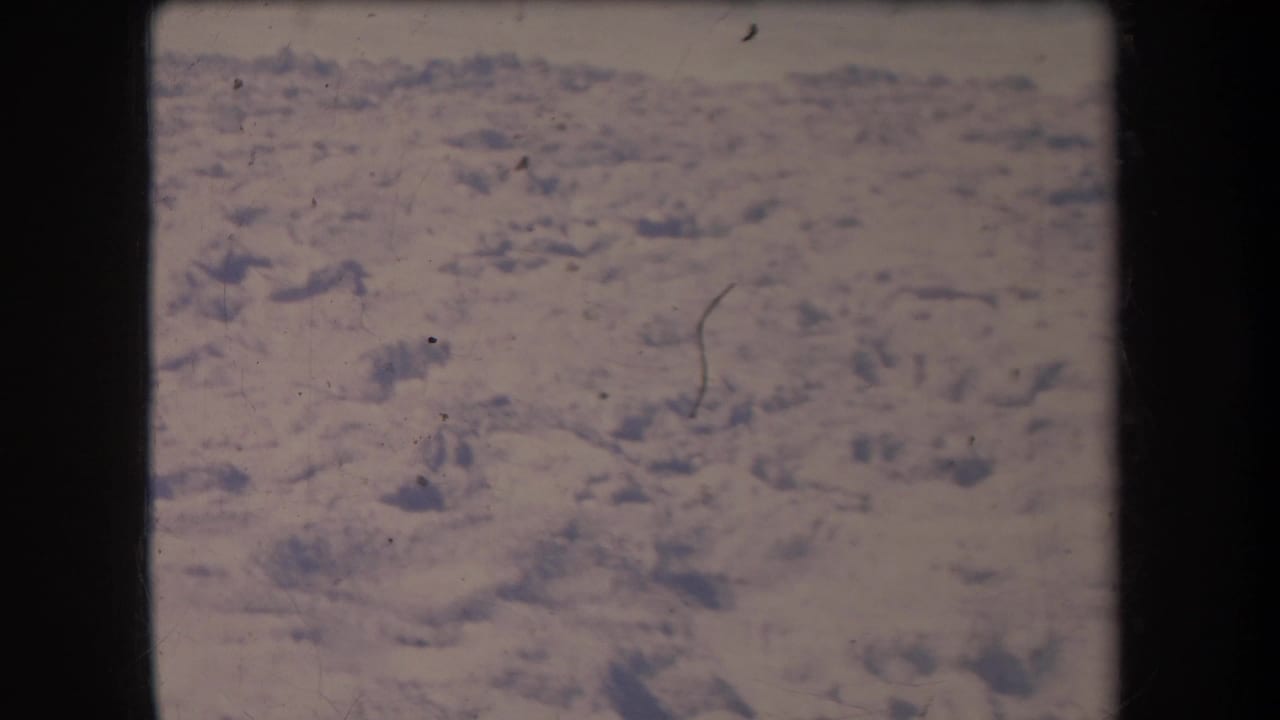 1969 Hawaii 8mm aerial frame showing pale, arid ground with scattered darker rocky areas, soft focus, and film wear.