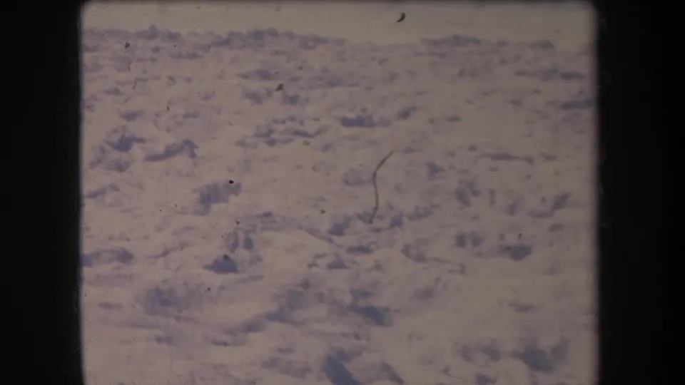 1969 Hawaii 8mm aerial frame showing pale, arid ground with scattered darker rocky areas, soft focus, and film wear.