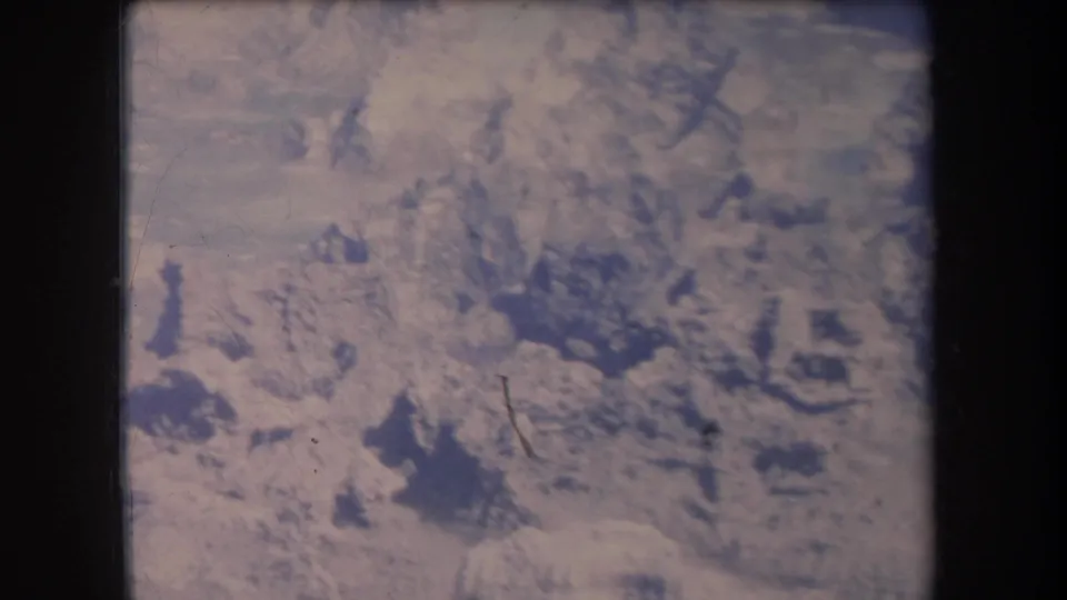 1969 Hawaii 8mm frame looking down on empty arid terrain, with pale ground, darker rocky forms, and visible film grain.