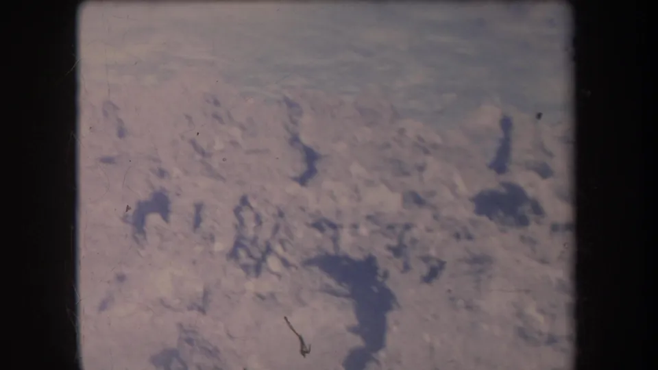 1969 Hawaii 8mm aerial view of barren pale ground with scattered dark terrain marks, soft exposure, and physical-film wear.