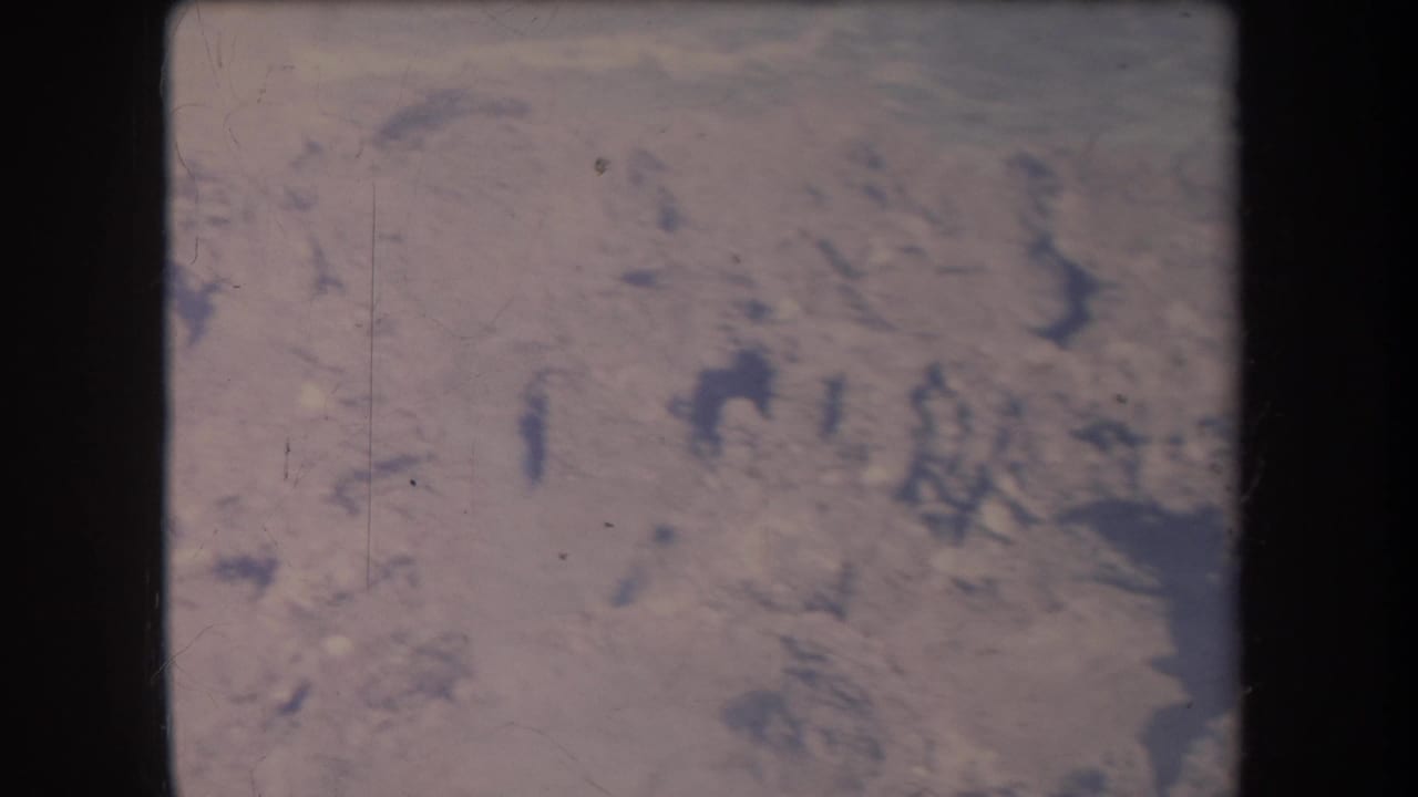 1969 Hawaii home-movie frame showing pale surf and dark coastal rocks in a soft, grainy 8mm scan.