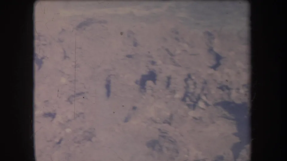 1969 Hawaii home-movie frame showing pale surf and dark coastal rocks in a soft, grainy 8mm scan.