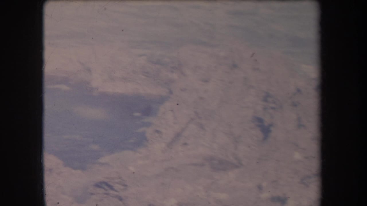 Overhead coastal view with foamy water moving around dark rock formations.