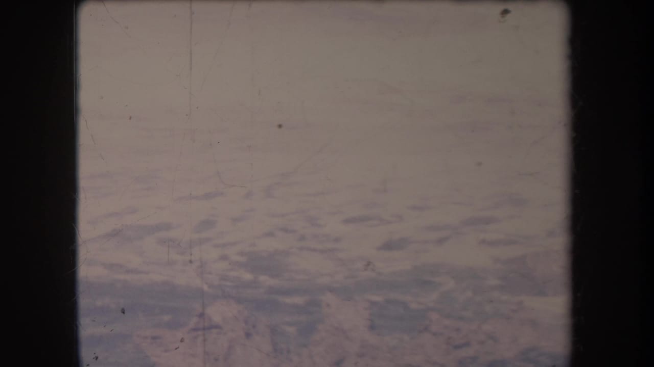 Soft aerial view of blue water and pale haze within an 8mm film frame.