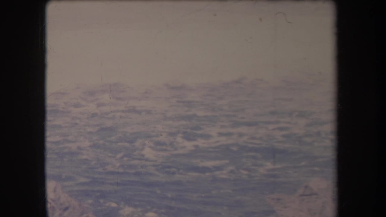 Aerial view over blue ocean with distant textured water and film gate edges.