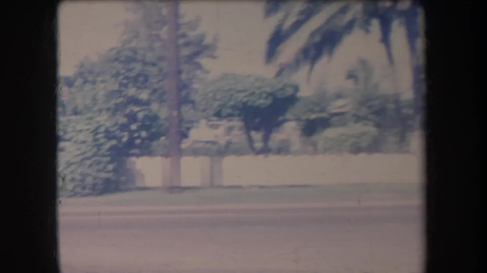 Late-1960s Hawaii footage shows a street-side view with palm trees, a white fence or wall, and dense residential landscaping.