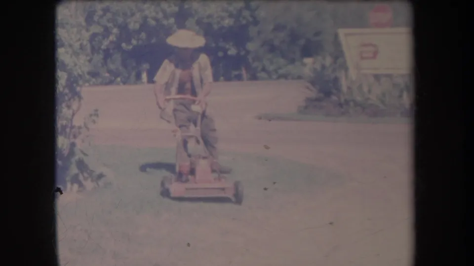 1969 Hawaii home-movie frame showing the man guiding the mower toward the camera across a sunlit lawn.